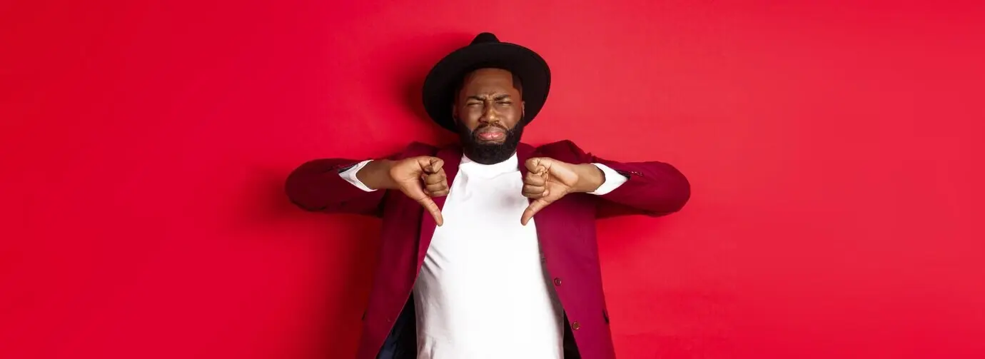 Enttäuschter schwarzer Mann hinterlässt negatives Feedback, zeigt den Daumen nach unten und verzieht vor Abneigung das Gesicht.